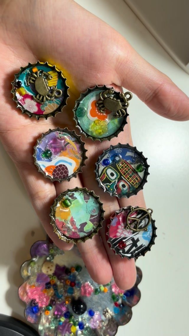 24 Art from Bottle Caps Ideas for Home, Gifts and Play 20 Six colorful resin art pieces made from bottle caps held in a hand.