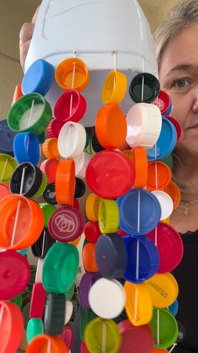 24 Art from Bottle Caps Ideas for Home, Gifts and Play 21 Colorful plastic bottle caps strung together hanging from a white plastic container.