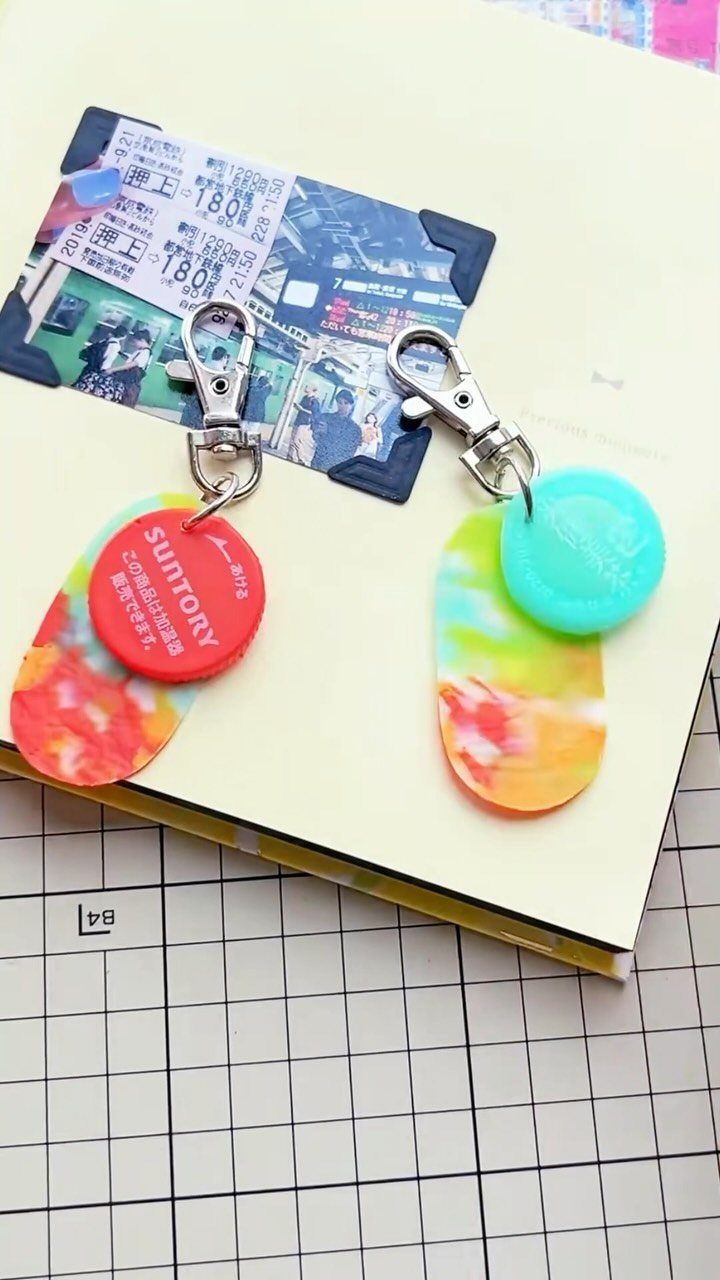 24 Art from Bottle Caps Ideas for Home, Gifts and Play 7 Two resin keychains with red and blue bottle caps on a yellow notebook.