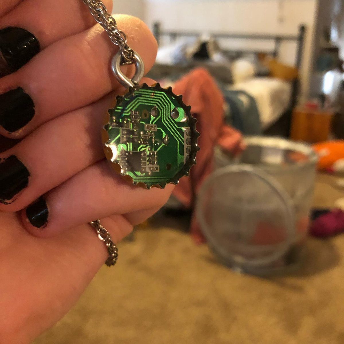24 Art from Bottle Caps Ideas for Home, Gifts and Play 5 Bottle cap necklace pendant containing a green circuit board held by a hand.