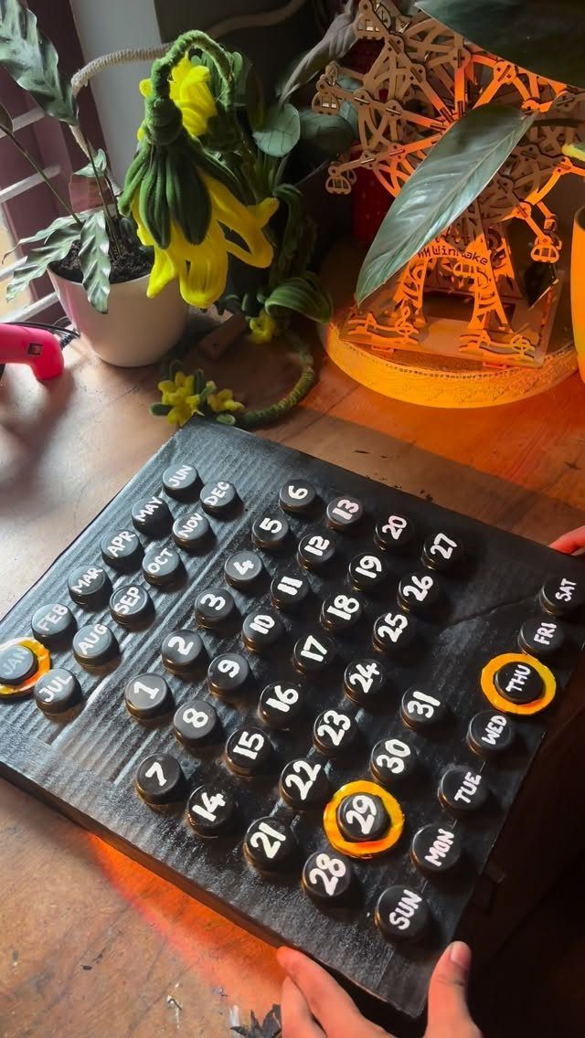 24 Art from Bottle Caps Ideas for Home, Gifts and Play 22 Handmade calendar made from black painted bottle caps on a black wooden board.