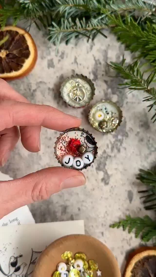 24 Art from Bottle Caps Ideas for Home, Gifts and Play 19 Hand holding a decorated bottle cap with the word JOY and red glitter.