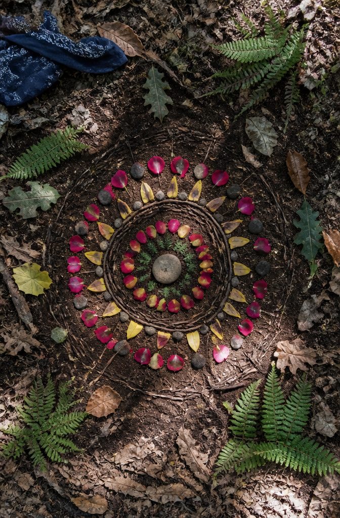 A nature mandala made of twigs, petals, and pebbles on the ground.