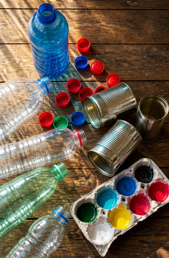 Recycled materials like plastic bottles, cans, and egg cartons on a workbench.