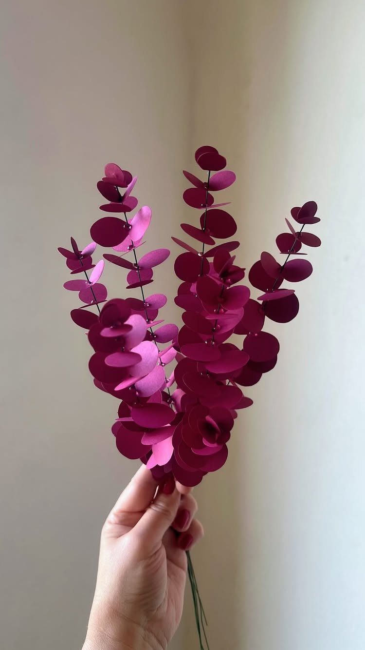 23 DIY Decor with Paper Projects for Every Room 7 Hand holding branches with small, round, deep magenta paper leaves against white wall.