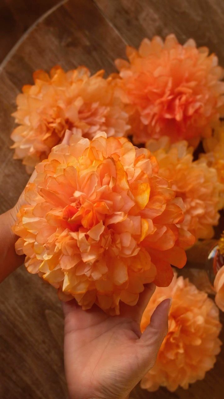 23 DIY Decor with Paper Projects for Every Room 13 Orange coffee filter flowers held in a hand over a wooden background.