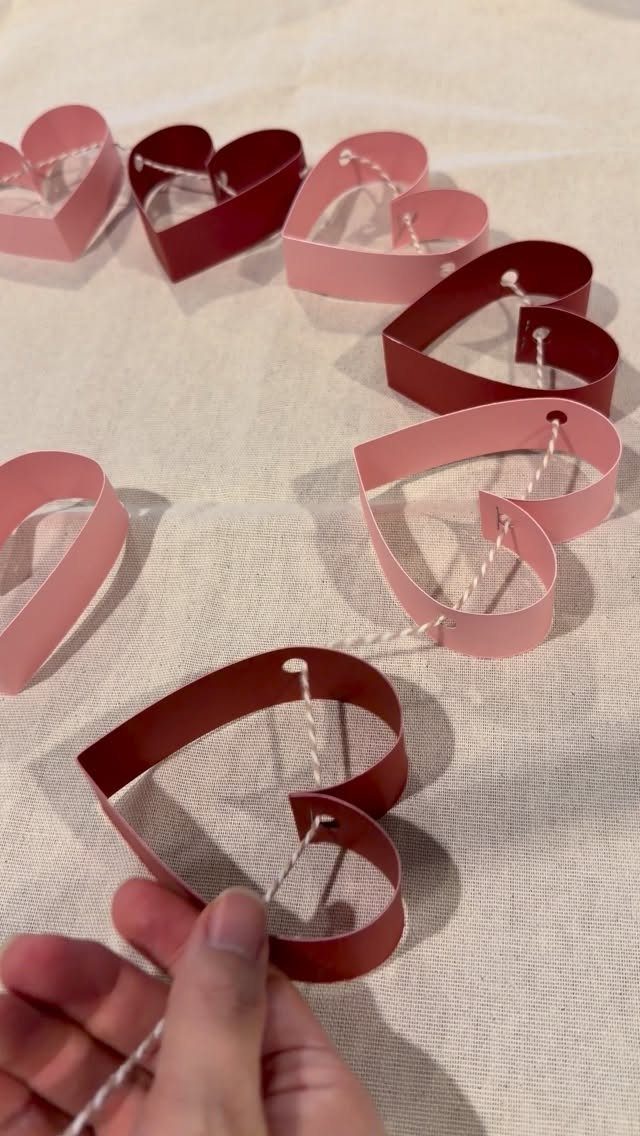 23 DIY Decor with Paper Projects for Every Room 1 Heart-shaped paper cutouts in pink and red strung together on a white thread.