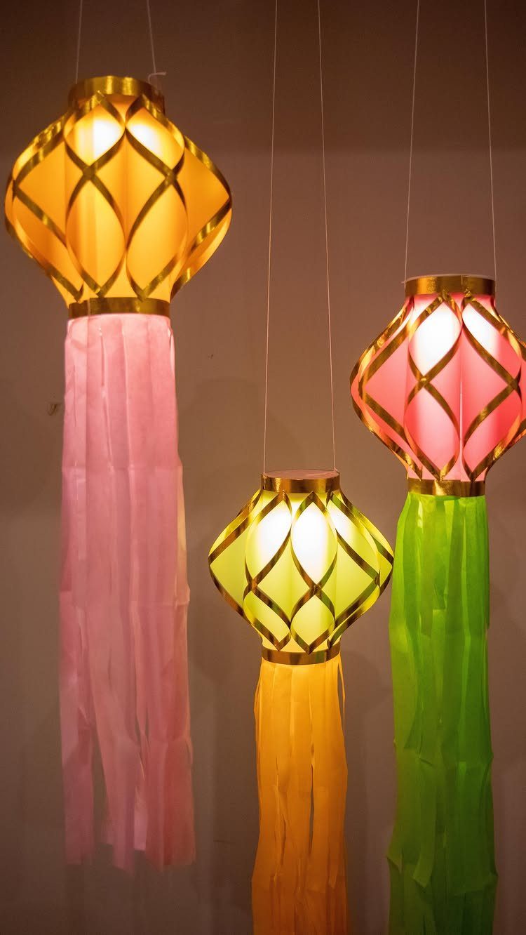 23 DIY Decor with Paper Projects for Every Room 11 Three colorful paper lanterns with gold diamond patterns and long hanging paper tassels.