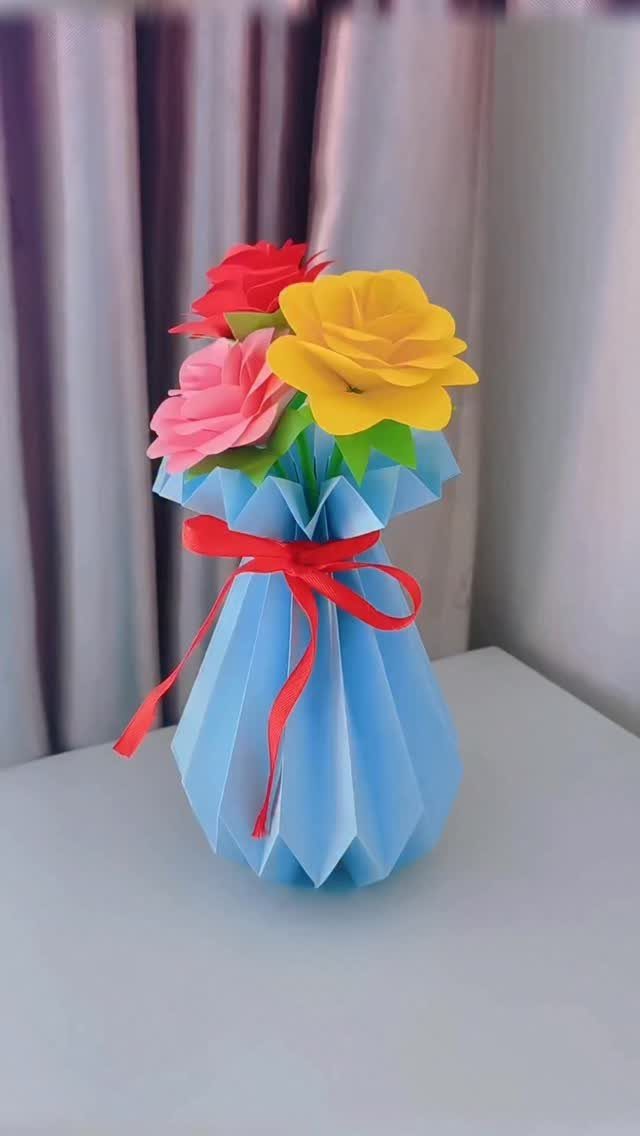 23 DIY Decor with Paper Projects for Every Room 3 Light blue pleated paper vase with red ribbon holding colorful paper roses.