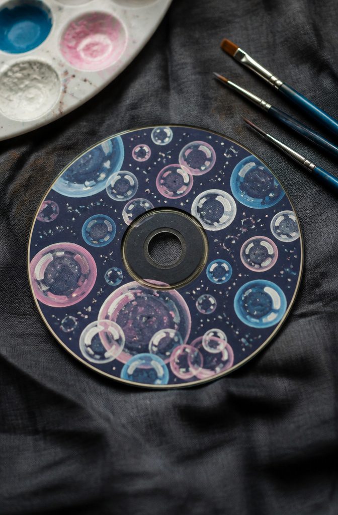 A CD featuring bubbles in white, light blue, and pink on a black surface.