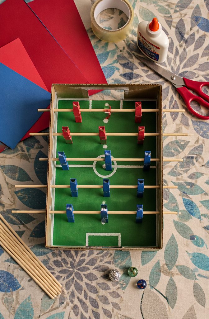 A shoebox-sized foosball table with green paper and wooden rods.