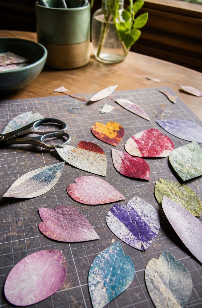 Workspace with different shaped painted newspaper petals and scissors.