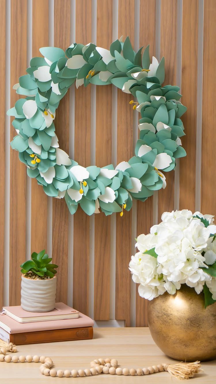 17 Recycled Art Projects for Kids and Adults to Make 1 Paper leaf wreath in green and white hanging on a wooden slat wall.
