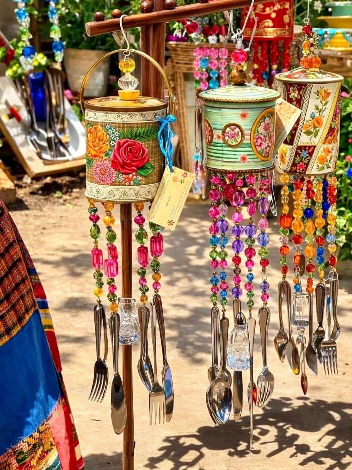 17 Recycled Art Projects for Kids and Adults to Make 2 Painted tin can wind chimes with colorful beads and silver cutlery hanging outdoors.